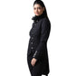 A woman modeling a black longline military-style jacket with ornate button details, a high ruffled collar, and matching black trousers against a plain white background.