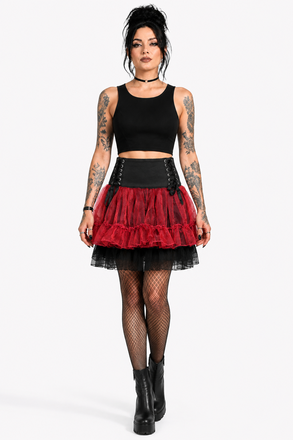 A model wearing gothic-style outfit featuring a black crop top, a black corset-style waistband, a red and black tiered tulle skirt, fishnet tights, and black platform boots, available for wholesale