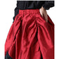 A close-up of a red satin-like skirt with a gathered elastic waistband, worn with a black top. A hand is visible at the side pocket of the skirt against a plain white background.