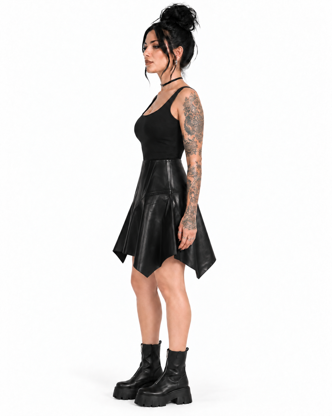 Side view of a model wearing a black PU handkerchief-hem skirt with a high panelled waist and uneven pointed drape.