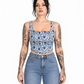 A woman with dark hair and tattoos models a blue and white patterned square-neck crop top with light-wash blue jeans against a plain white background.